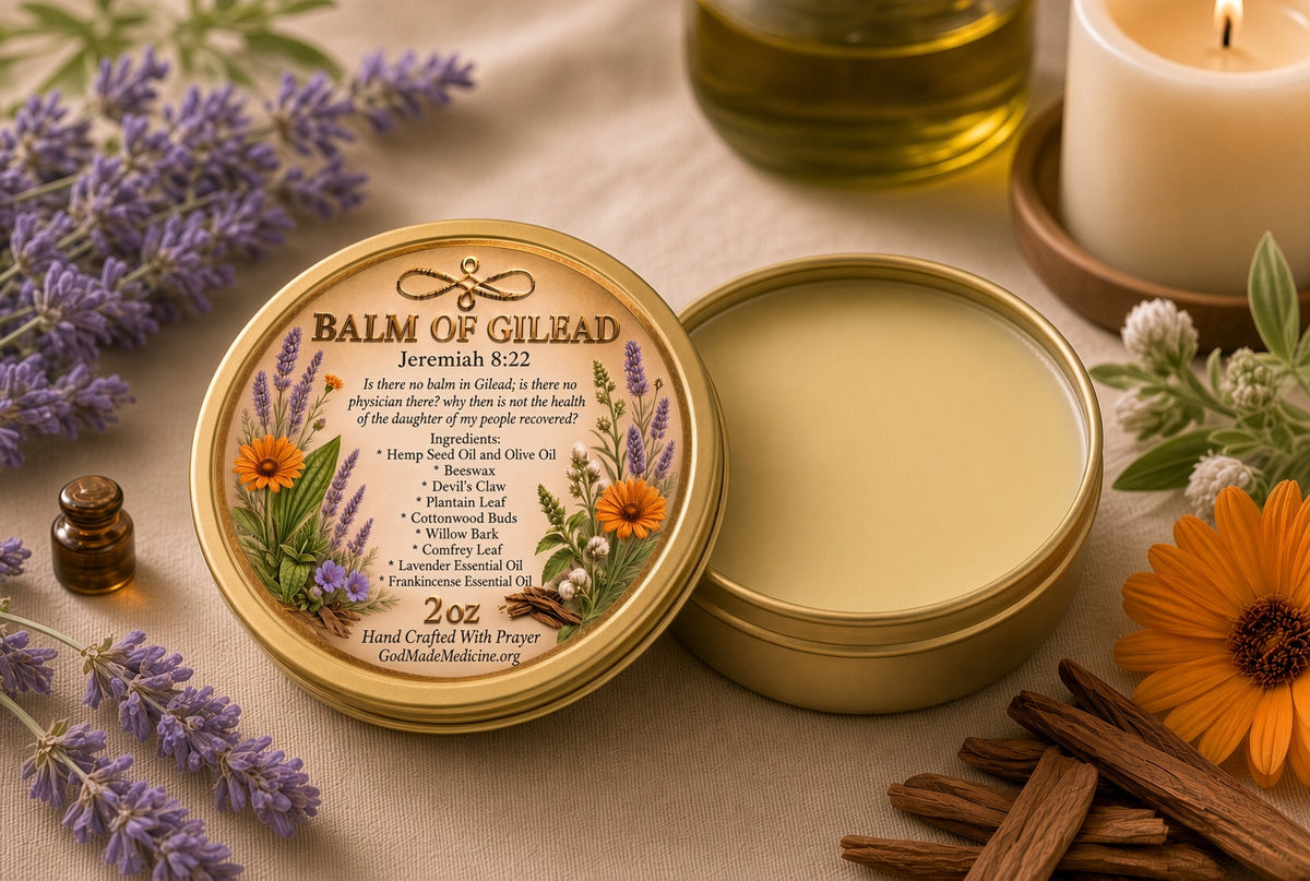An open round tin of Balm of Gilead sits on a beige fabric surface with lavender sprigs, cinnamon sticks, an orange flower, a small bottle, and candles around it. The lid label shows botanical illustrations and product text, and the balm inside is a pale yellow cream